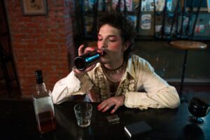 A person dressed in vintage style sipping from a beer bottle in a dimly lit bar.