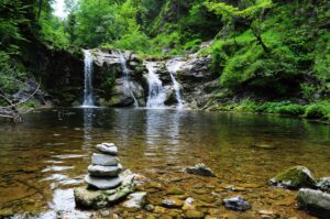 My Personal Gay Stories Peaceful forest waterfall with serene stone cairn, ideal for nature and travel themes.