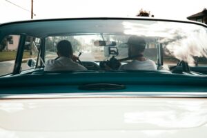Two filmmakers capturing scenes from a vintage car interior.