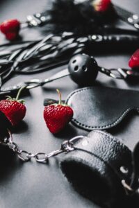 Close-up of black leather BDSM gear with strawberries, creating a sensual atmosphere.