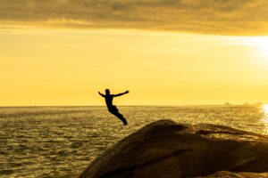 A fearless man jumps off a cliff into the ocean during a stunning golden sunset, symbolizing freedom and adventure.